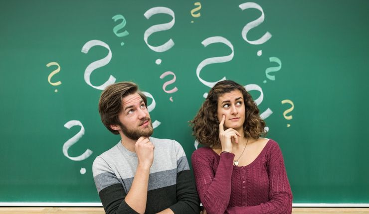 Ein Student und eine Studentin stehen vor einer Tafel mit angezeichneten Fragezeichen, Foto: Christian Hüller