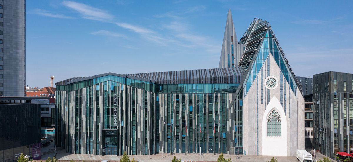 Die Glasfassade des Neuen Augusteums, abgebildet aus Richtung des Augustusplatzes, vor einem blauen, sommerlichen Himmel.