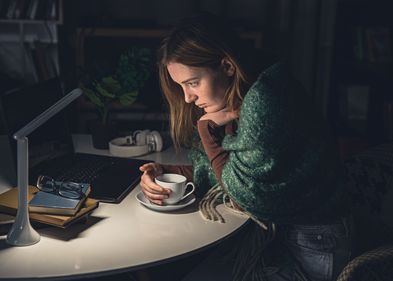 Eine Frau sitzt lustlos und mit einer Tasse in der Hand vor dem Laptop.