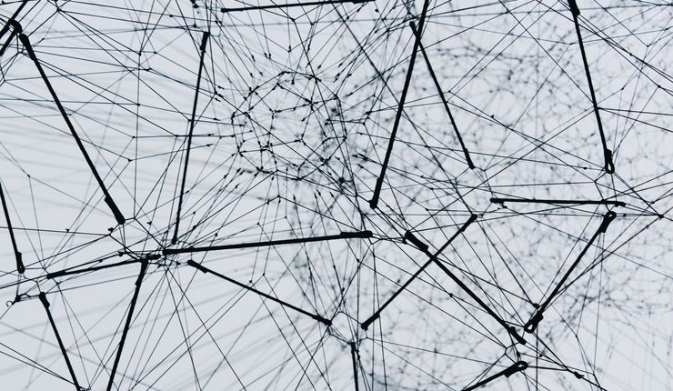 Ein Foto von einem Netzwerk von dunklen Kabeln oder Fäden vor einem hellgrauen Hintergrund. Obwohl es sich um eine Fotografie handelt, sorgt der hohe Kontrast für einen eher abstrakt-geometrischen Effekt. Das Foto steht als Symbolbild für neuronale Netzwerke.