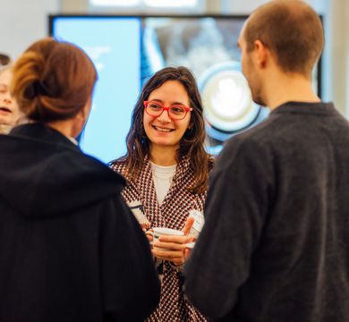Woman smiling and holding a cup is talking to other people