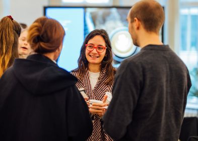 Woman smiling and holding a cup is talking to other people