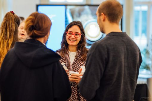 Woman smiling and holding a cup is talking to other people