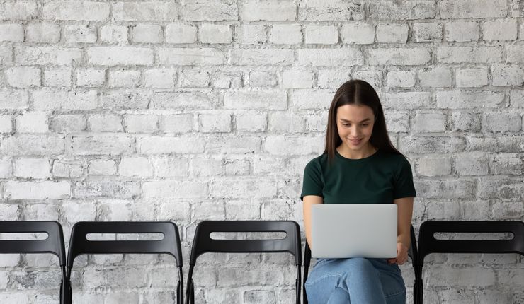 Zu sehen ist eine sitzende junge Frau, die an ihrem Laptop arbeitet