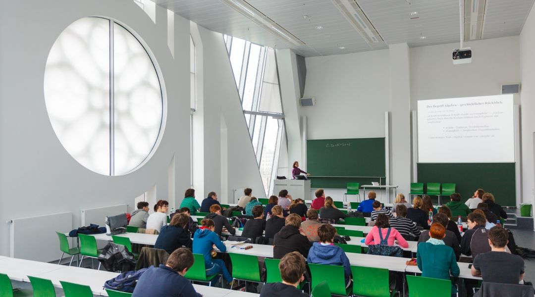 Foto: Studierende während einer Vorlesung in einem Hörssal mit grünen Stühlen